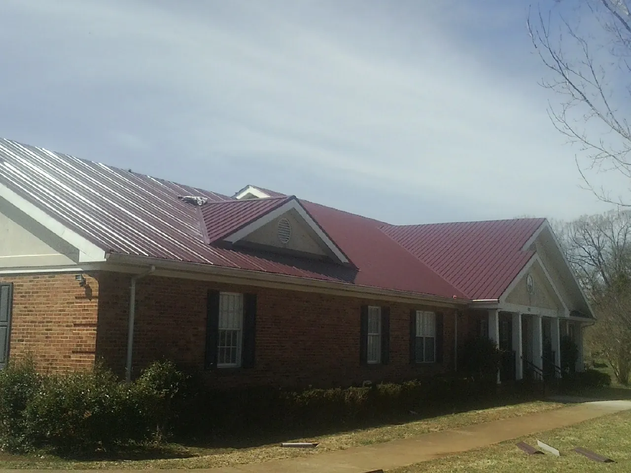 Red metal roof with gabled entries on a long brick building, from a Hail Damage Roof Repair job in Magnolia